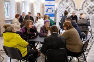 Jeweils sechs Teilnehmer der „Lebendigen Bibliothek“ in einem ehemaligen Ballsaal in den Räumlichkeiten der Caritas Mariupol tauschen sich an einem Tisch miteinander aus. Die in jeder Gruppe vertretenen Experten werden hier auch als „Lebendige Bücher“ bezeichnet.