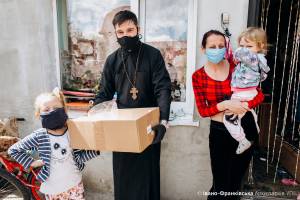 Ein Freiwilliger bringt einer Mutter mit ihren zwei Kindern ein Essenspaket, alle tragen Mund-Nase-Masken.