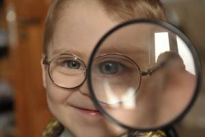 Ein Kindergartenjunge schaut durch eine große Lupe und hat ein vergrößertes Auge.