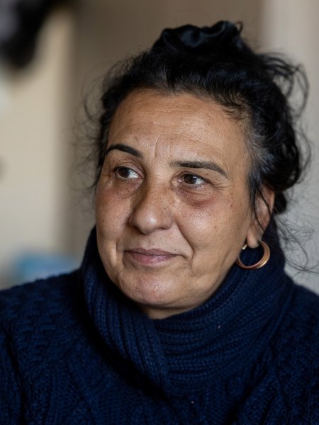 Porträt von Elena, der 56jähigen Romnja, die im Concordia-Zentrum Unterstützung bekommt. Elena trägt einen dunkelblauen Strick-Pullover, die dunklen, lockigen Haare sind im Nacken zusammengenommen, ihre Ohrringe glänzen.